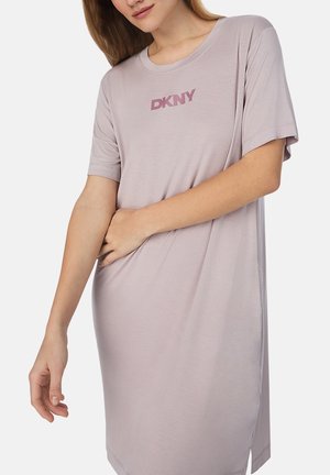 Frau trägt ein locker sitzendes, helllila DKNY-Kurzarmkleid mit rundem Ausschnitt, stehend vor einem schlichten weißen Hintergrund.