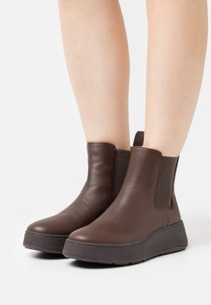Bottes chelsea en cuir marron avec des panneaux élastiques sur les côtés, un bout rond et une semelle épaisse en wedge pour plus de hauteur et de confort.