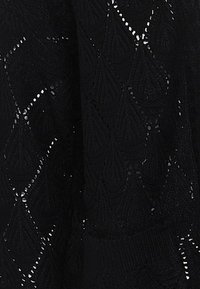 Maglione in pizzo nero caratterizzato da un motivo a foglia testurizzato, con dettagli a lavoro aperto e un orlo aderente, che mette in mostra un'artigianalità intricatissima.