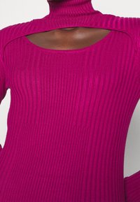 Pull côtelé ajusté en fuchsia vif, avec un col montant et une épaule dénudée, présentant une texture verticale et une coupe près du corps.