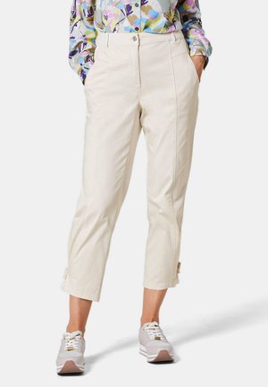 Pantalons beiges cropped avec poches avant, devant plat et liens latéraux subtils. Assortis à des baskets gris clair avec des accents blancs.