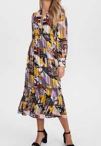 Robe multicolore avec un mélange de motifs géométriques et floraux. Manches longues, col en V, longueur au genou avec un ourlet à volants et une taille élastique.