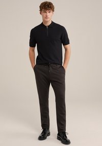 Black short-sleeve polo with a front zipper and pocket, paired with dark gray tapered trousers and black lace-up shoes. Smooth fabric texture.