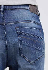 Tummansiniset farkut, joissa on haalistunut pinta, varustettuna kahdella takataskulla ja ruskealla nahkabrändileimalla vyötärön lähellä.