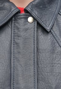 Marineblauwe leren jas met een gestructureerd oppervlak, een opvallende kraag en zilveren drukknoop met contrasterende blauwe stiksels.