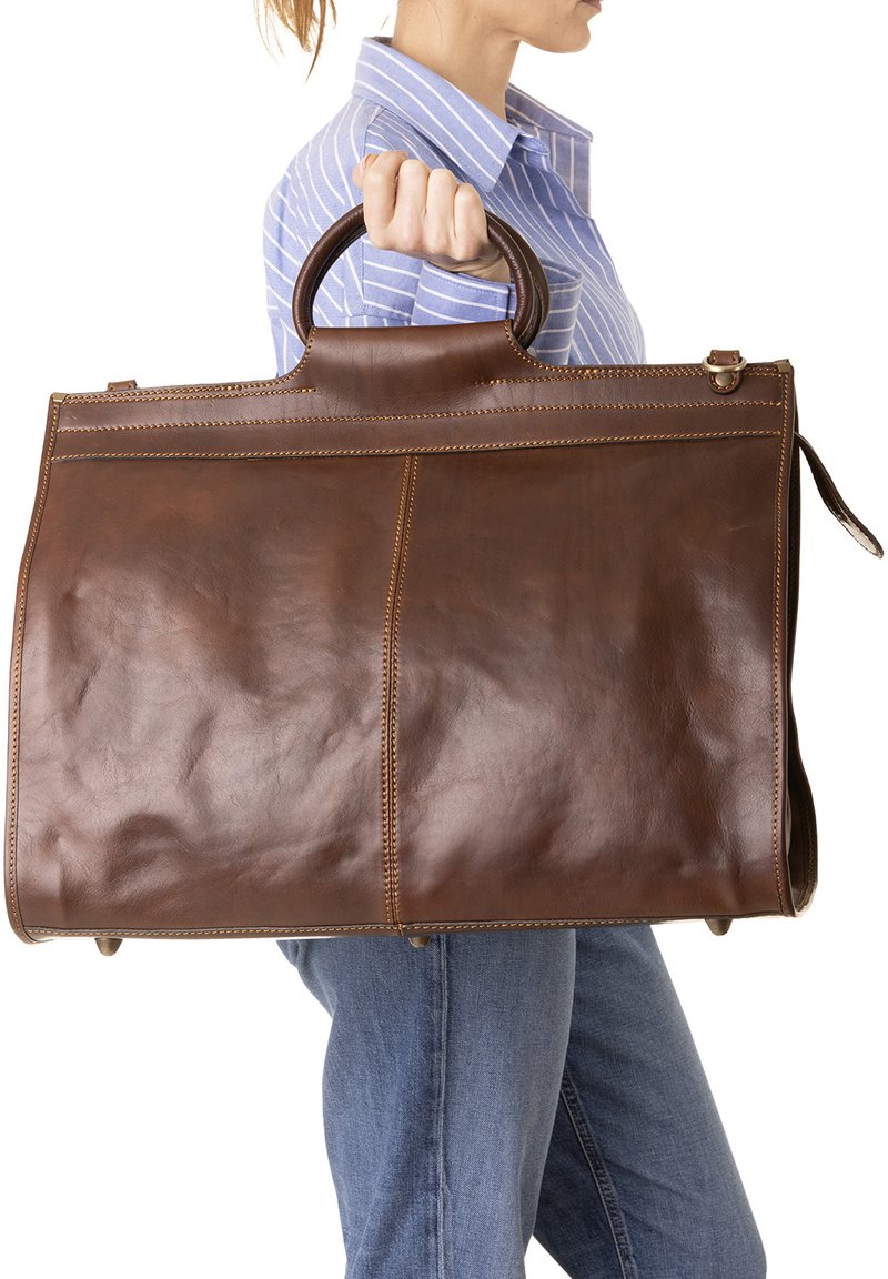 Borsa a tracolla in pelle marrone con una texture liscia, dotata di una maniglia superiore e cuciture contrastanti, tenuta da una persona in abbigliamento casual.