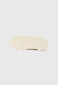 Footwear outsole features a textured, cream-colored rubber with a geometric pattern and traction grooves for grip and durability.