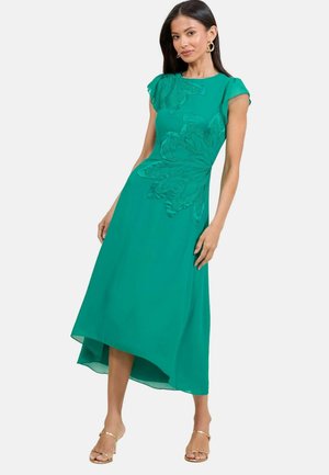 Taidemittainen teal-mekko, jossa on hihattomat hihat, silkkimäinen rakenne ja kukka-applikaatio edessä, asennossa epäsymmetrinen helma ja liukuvat muotoilu.