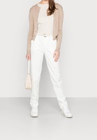 Cardigan beige sur une chemise rayée, pantalon blanc taille haute, baskets blanches et un petit sac à main beige texturé. Design simple et épuré.