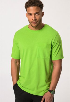 Camiseta de manga corta verde brillante hecha de una tela suave, con un bolsillo en el frente, cuello redondo y un corte relajado. Combinada con pantalones negros.