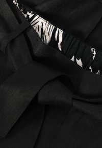 Tissu noir avec une ceinture nouée, montrant une taille élastique avec un motif zèbre noir et blanc à l’intérieur.