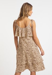 Blommig klänning i beige med bruna leopardfläckar, med ett lager-på-lager design och justerbara knytband. Slät tygkvalitet.