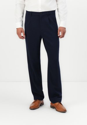Pantalons tailleur bleu marine avec un devant plat, des jambes pliées, et une fermeture à bouton unique, assortis à des chaussures habillées marron.