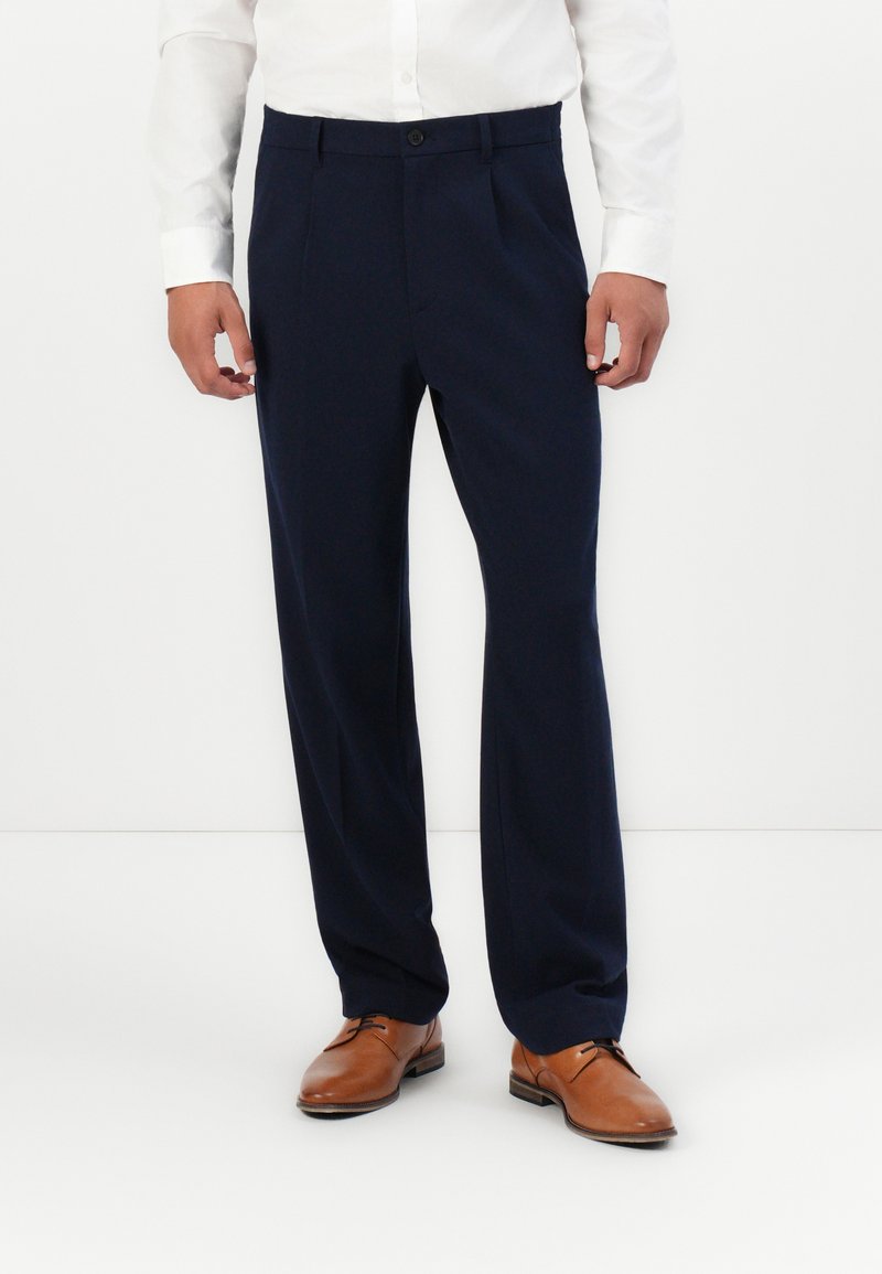 Pantaloni ajustați de culoare bleumarin, cu față netedă, picioare pliate și închidere cu un singur nasture, asortați cu pantofi de dress maro.
