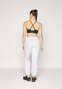 Reggiseno sportivo nero con spalline incrociate, abbinato a pantaloni sportivi grigi chiari e scarpe da ginnastica nere.