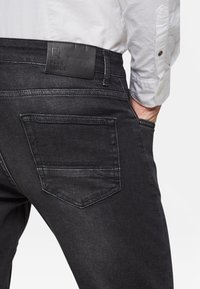 Svarta denimjeans med en läderlapp märkt "BLUE RIDGE" vid midjan, med en enda bakficka med subtila sömdetaljer.