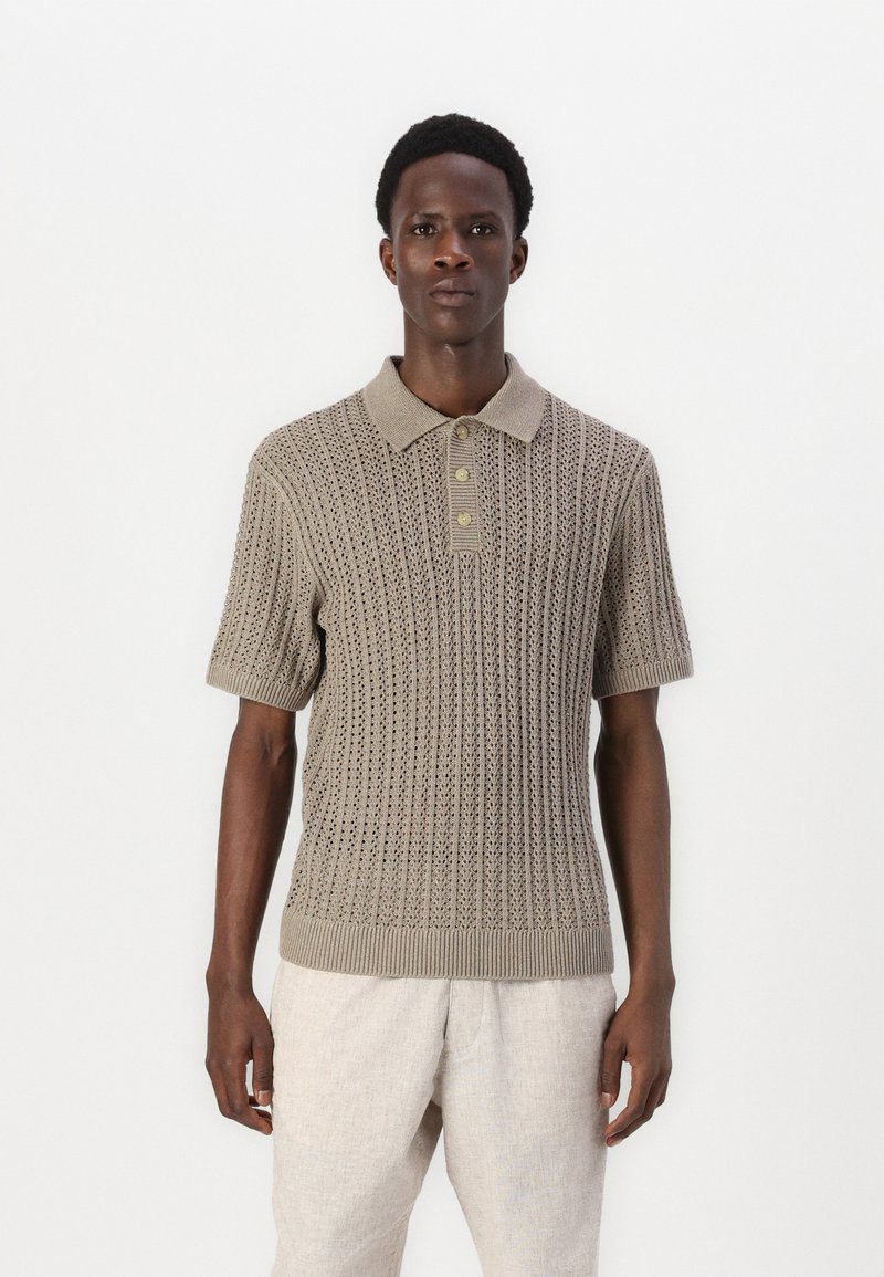 Stickad polo i beige med ett texturerat mönster, med ribbat krage, korta ärmar och tre knappar vid halsringen.