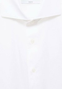 Camicia bianca slim-fit con colletto standard, pattina verticale e bottoni trasparenti. Tessuto morbido con una finitura liscia.