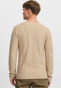 Beige Pullover mit langen Ärmeln, der über ein strukturiertes Strickdesign und einen runden Halsausschnitt verfügt; enganliegende Ärmel enden am Handgelenk, mit einem geraden Saum auf Taillenhöhe.