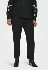 Melna krekliņa ar pogām un ziedu izšuvumu uz piedurknēm, apvienots ar melniem piegrieztiem biksēm un potīšu zābakiem. Gluda auduma, pielāgota piegriezuma.