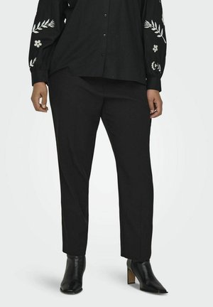 Chemise noire à boutons avec broderie florale sur les manches, associée à un pantalon noir ajusté et des bottines. Tissu lisse, coupe ajustée.