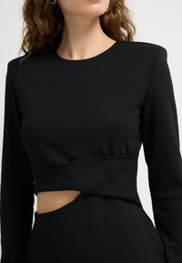 Sort langærmet kjole med udskæring i taljen, lavet af glat stof med en tætsiddende pasform og rund halsudskæring.