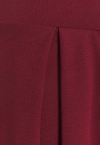 Tessuto bordeaux con una texture liscia che presenta un design plissettato, evidenziando linee verticali e una leggera lucentezza nel materiale.