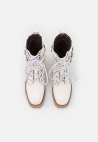 Botines de piel blanca hasta el tobillo con punta redonda, material texturizado, cordones grises y clavos decorativos de metal. Suelas de goma con un ligero agarre.