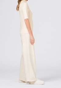 Krémový krátký rukáv top v kombinaci s širokými kalhotami ve stejném odstínu. Oba mají hladkou texturu a volný střih, doplněné o bílé tenisky.