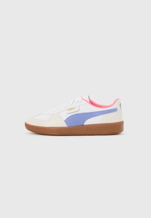 Biały niski sneaker z niebieskim paskiem Puma, różową wyściółką, gumową podeszwą i złotą etykietą Puma Palermo po boku.