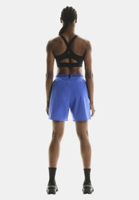 Schwarzer Sport-BH mit Ausschnitt-Design auf dem Rücken, kombiniert mit blauen Sportshorts. Die Shorts verfügen über einen elastischen Bund und ein leichtes Material.