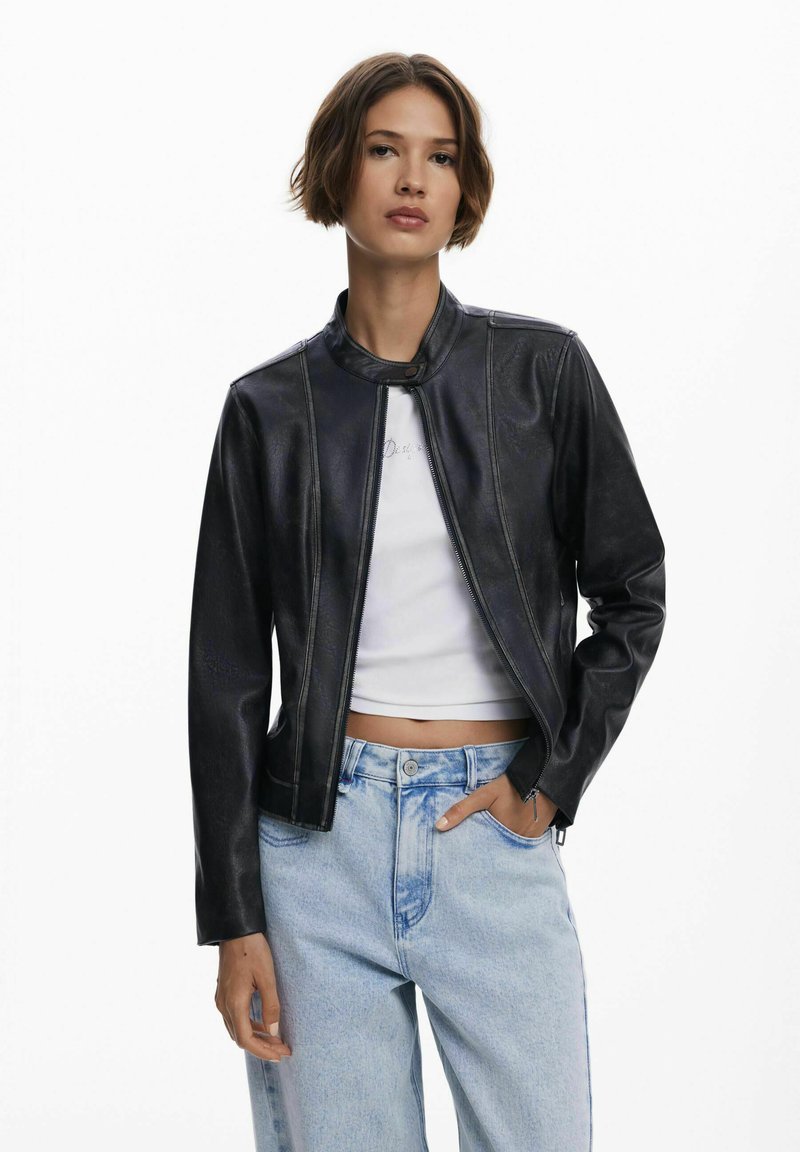 Zwarte leren cropped jack met een opstaande kraag, ritssluiting aan de voorkant en lange mouwen. Gecombineerd met lichtblauwe high-waisted jeans.