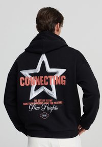 Felpa nera con cappuccio caratterizzata da una grande grafica di una stella bianca sul retro, la scritta "CONNECTING" in corallo e frasi decorative. Tessuto morbido con una vestibilità comoda.