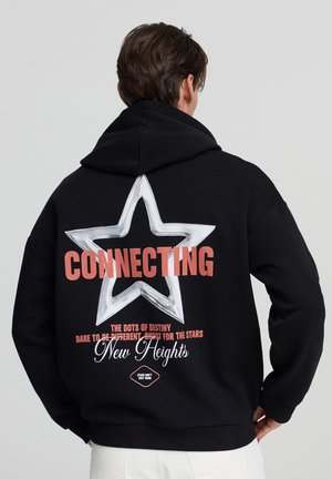 Felpa nera con cappuccio caratterizzata da una grande grafica di una stella bianca sul retro, la scritta "CONNECTING" in corallo e frasi decorative. Tessuto morbido con una vestibilità comoda.