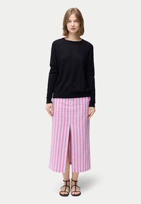 Schwarzes, strukturiertes Langarmoberteil kombiniert mit einem rosa gestreiften Midirock mit zentralem Schlitz. Modell trägt schwarze, Riemchensandalen.