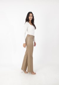 Beige, hoog-getailleerde flare broek gemaakt van rekbaar materiaal, met achterzakken en een gladde afwerking, gecombineerd met een aansluitend wit langmouwen shirt.