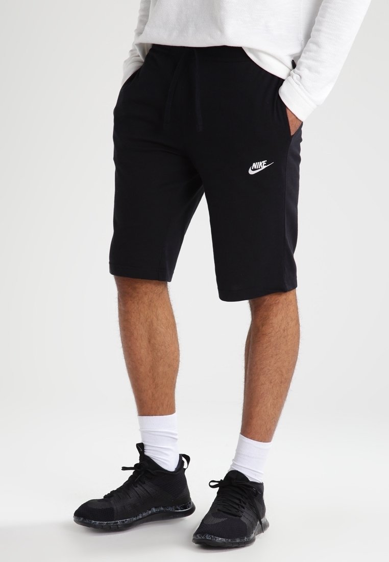 Svarta Nike-shorts med elastisk midja, prydda med en vit logotyp. I kombination med svarta träningsskor och vita strumpor. Tyget är en blandning av bomull.