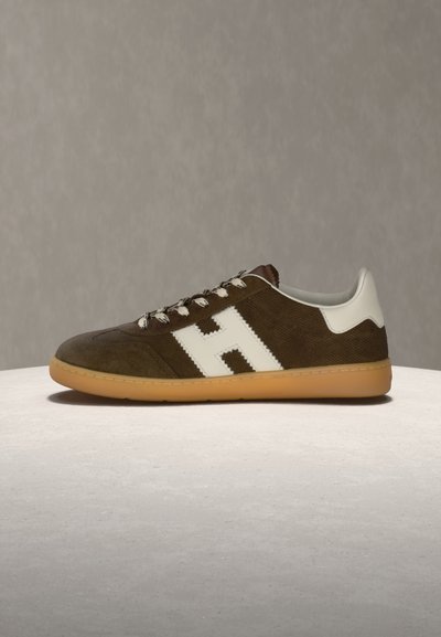 Καφέ σουέντ αθλητικό παπούτσι με λευκό λογότυπο "H", λευκή έμφαση στη φτέρνα, κορδόνια με μοτίβο και σόλα από καουτσούκ σε χρώμα καραμέλας, τοποθετημένο πάνω σε ανοιχτόχρωμη υφασμάτινη επιφάνεια.