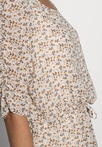 Losse, kortdurende blouse van lichtgewicht stof met een crèmekleurige achtergrond, voorzien van een bloemenpatroon in oranje en zwart.