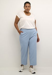 Pantalones azul claro a medida con una textura suave, bolsillos laterales y un corte relajado, combinados con una camisa blanca de manga corta y zapatillas.