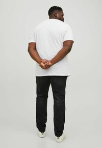 White short-sleeve t-shirt, relaxed fit, paired with dark jeans and white sneakers. Plain design, solid colors, no visible patterns or logos.