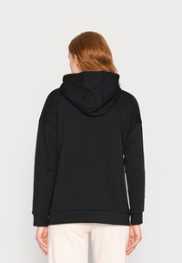 Sweat à capuche noir avec une coupe décontractée, des poignets côtelés et un tissu texturé. Détails de couture visibles sur le dos et la capuche.