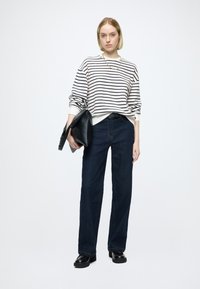 Bluza w paski w kolorze białym i czarnym, zestawiona z ciemnoniebieskimi szerokimi spodniami i czarną torebką. Gładka tkanina, swobodny krój, minimalistyczny design.