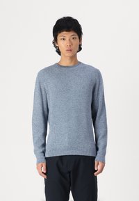 Suéter de punto texturizado azul con mangas largas, cuello redondo y puños acanalados. Combinado con pantalones oscuros sobre un fondo blanco liso.