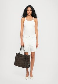 Débardeur blanc, short en denim blanc et chaussures beiges à bout pointu. Sac fourre-tout en cuir crocodile marron foncé avec des poignées noires.