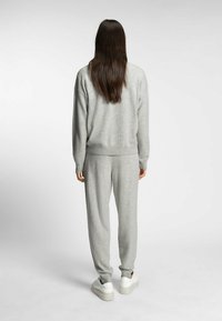Grauer Pullover und Jogginghose-Set aus weichem Stoff. Verfügt über eine lockere Passform, gerippte Bündchen und eine glatte Textur. Weiße Sneakers runden den Look ab.