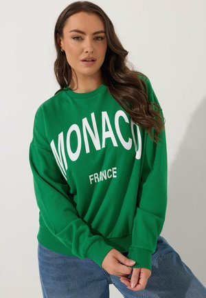 Grüner Pullover mit weißen Schriftzügen "MONACO" und "FRANKREICH", mit Rundhalsausschnitt und gerippten Bündchen. Weicher, lässiger Stoff.
