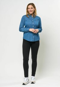 Denim overhemd met knopen in middentonen blauw, met een kraag en knopenlijst, gecombineerd met zwarte slim-fit broek en lichte sneakers met een zilveren accent.