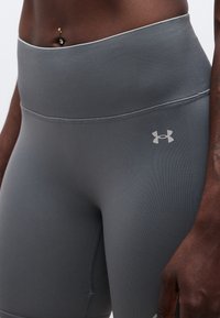 Κοντινό πλάνο ατόμου που φοράει γκρι σφιχτό κολάν Under Armour με ψηλή μέση, με ένα σκουλαρίκι στην κοιλιά να φαίνεται πάνω από τη μέση του κολάν.