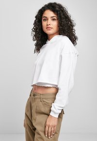 Bela skrajšana kapa z robom brez zaključka, dolgimi rokavi in rebrastimi manšetami, kombinirana s svetlo rjavimi hlačami z visokim pasom in sprednjimi žepi.